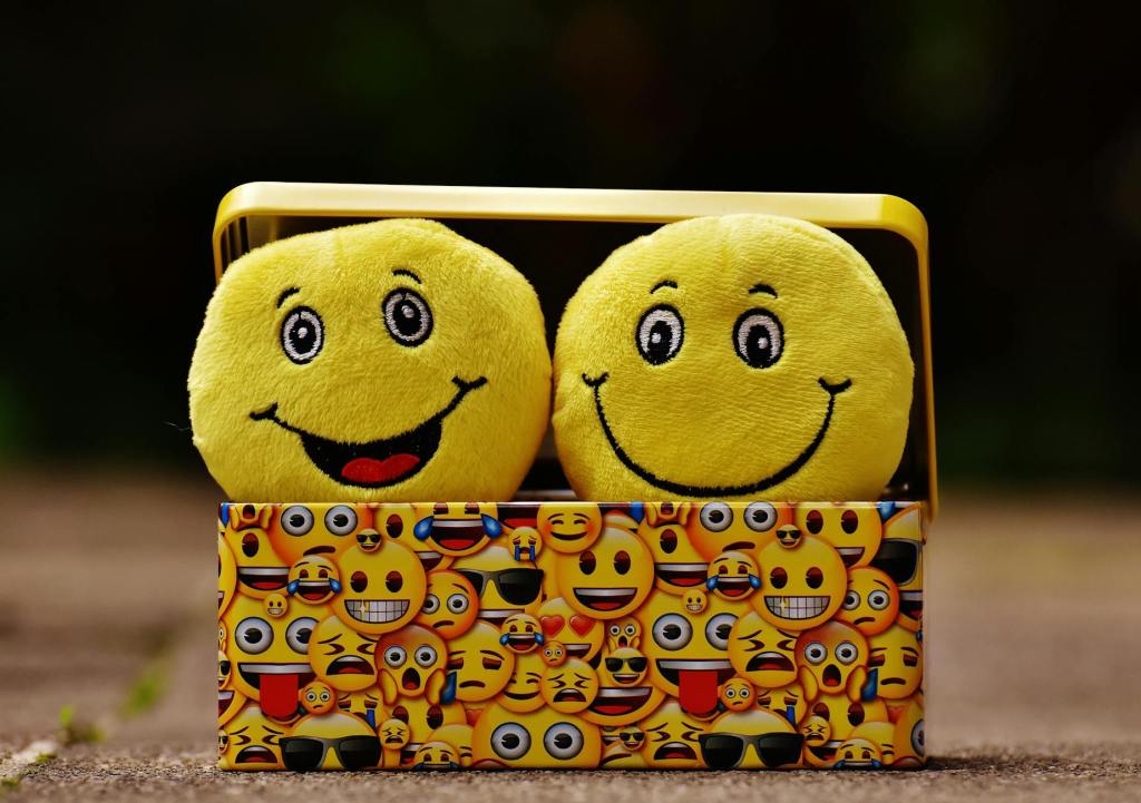 Two yellow smiley-face toys in a colourful emoji-patterned box, representing the emotions behind our relationship with money.