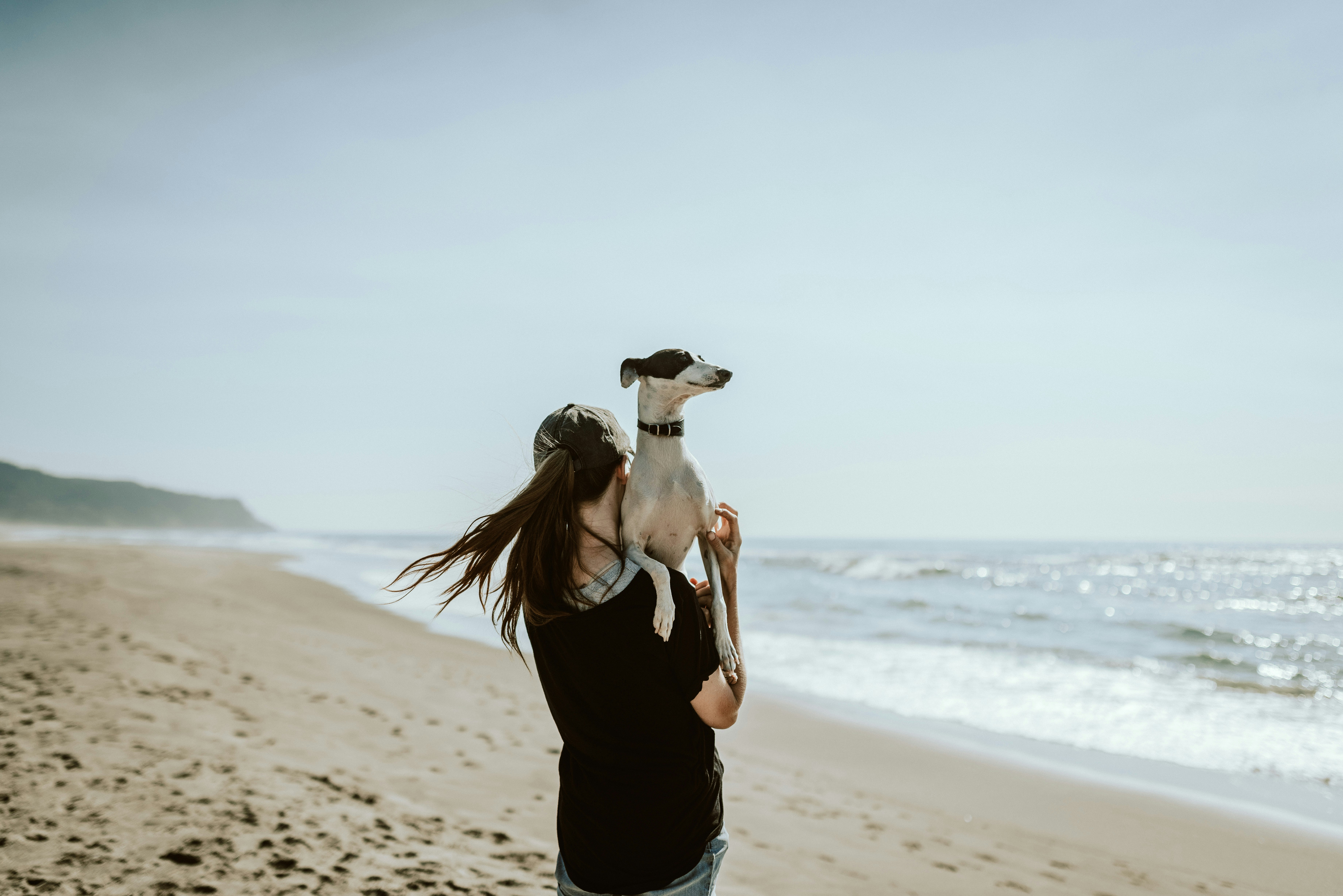 Woman standing on a beach holding her dog, representing freedom, calm and confidence with money.