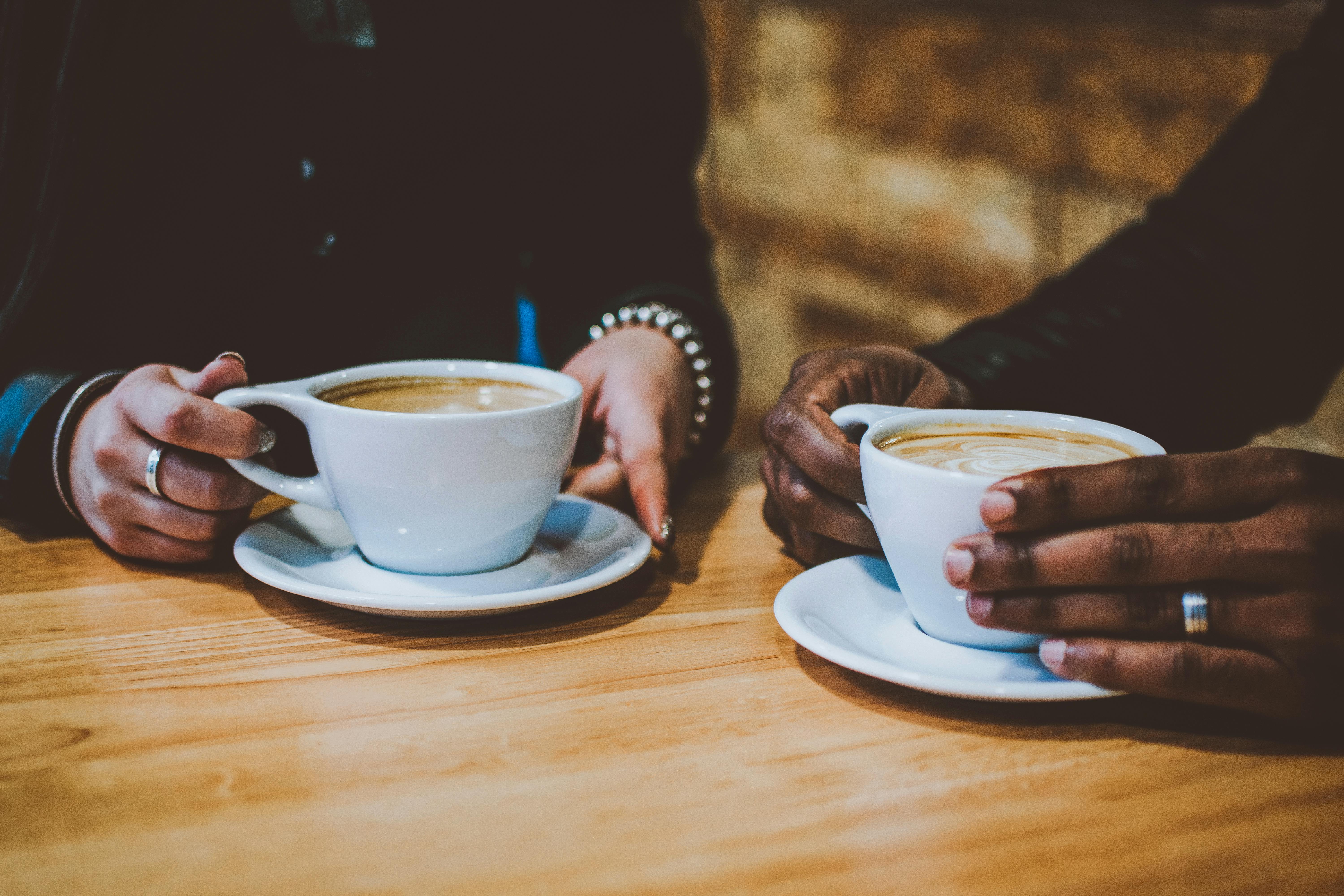 Two women sitting in a café holding coffee cups, symbolising supportive conversations about money and mindset.