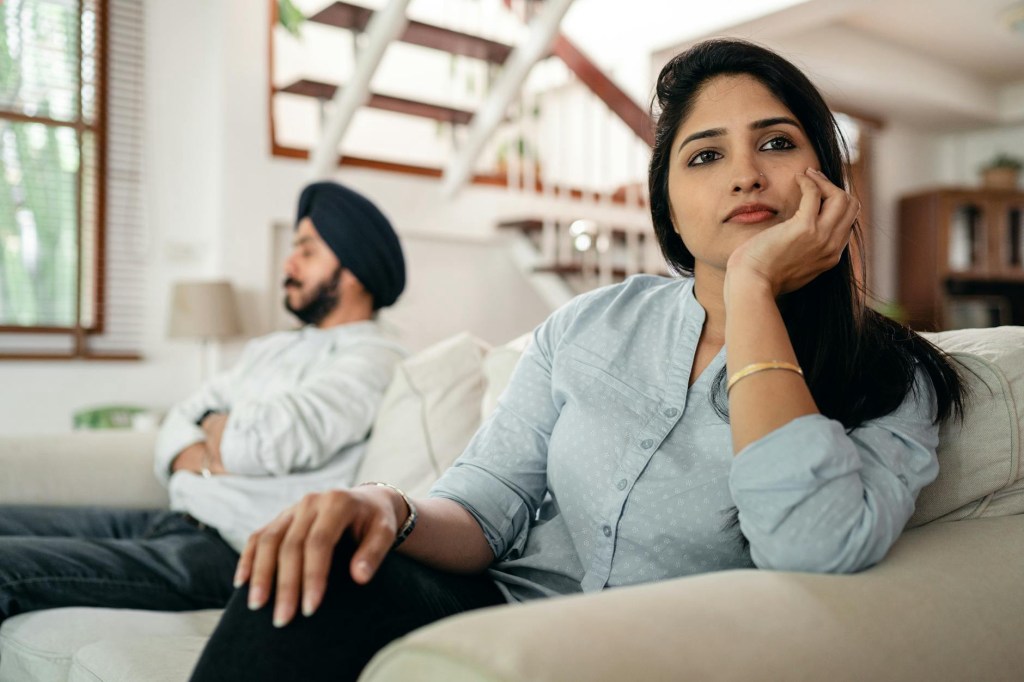 Woman sitting on a sofa deep in thought with partner in the background, symbolising avoidance and awareness in financial wellbeing.
